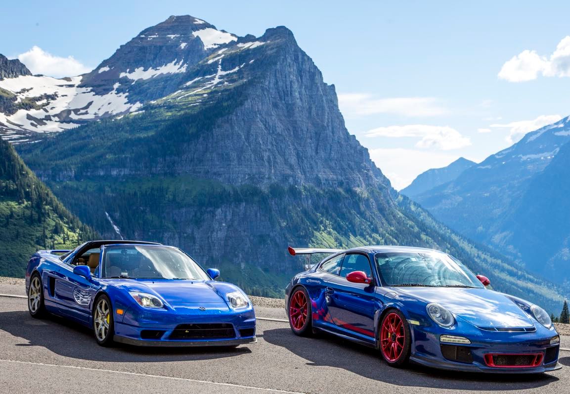 Two blue sports cars parked in front of a mountain in Glacier National Park
