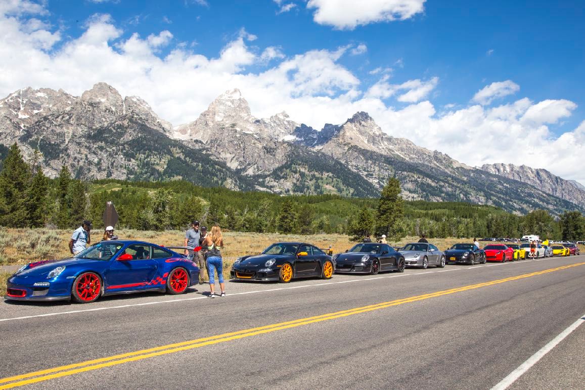 A line of Porsches and other sports cars parked along the road below the Grand Tetons